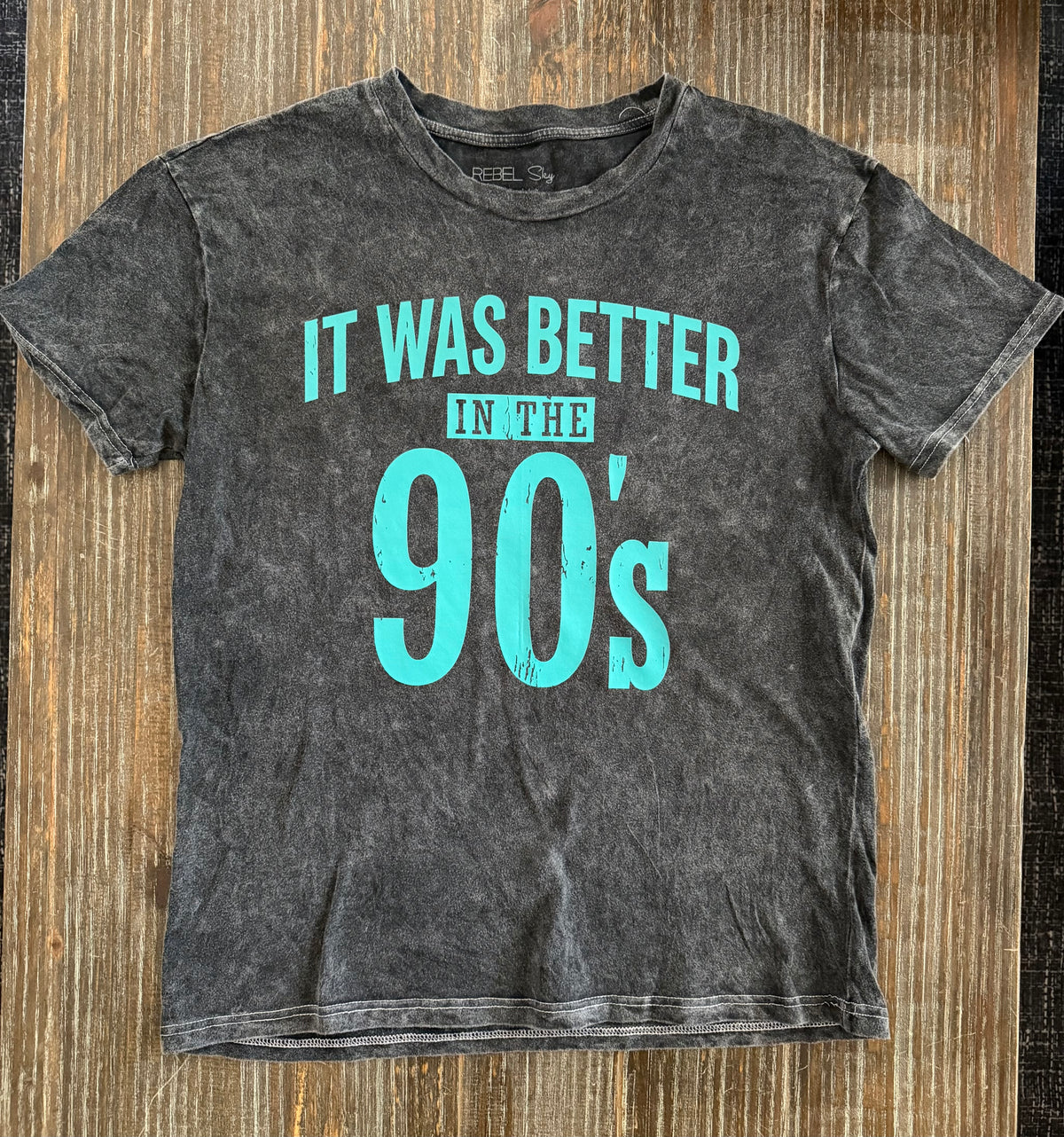 Black vintage-style t-shirt with turquoise 'It Was Better In The 90's' graphic on wooden surface